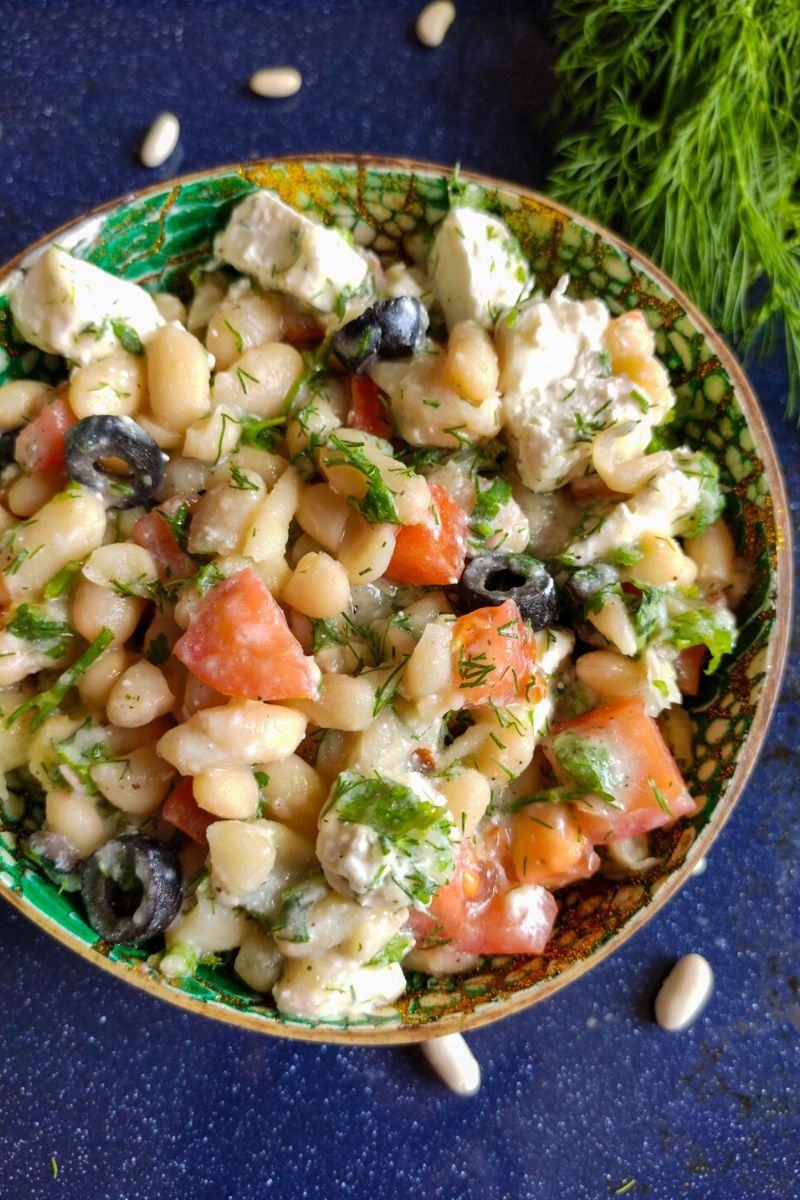 Mediterranean white bean salad served in a green bowl with fresh dill and dried white beans in the background