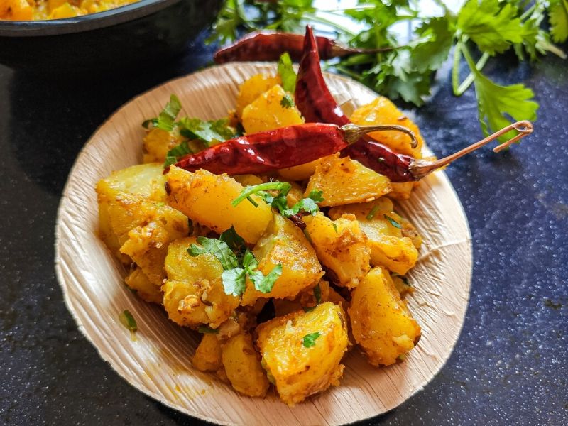 Pan fried potatoes garnished with fried chilies and coriander leaves served in a small wooden bowl