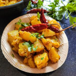 Pan fried potatoes garnished with fried chilies and coriander leaves served in a small wooden bowl