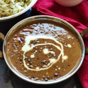 Dal makhani garnished with cream served in a bowl with some rice in the background