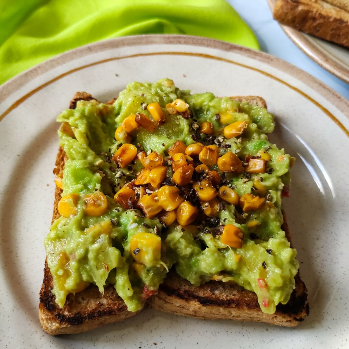 vegan avocado toast with pineapple and sweetcorn served on a plate kept on a bright green table napkin