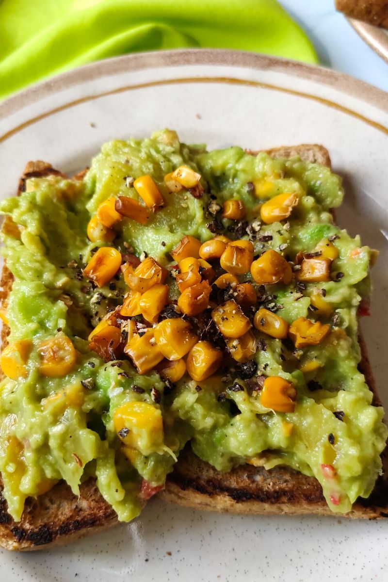 vegan avocado toast with pineapple and sweetcorn served on a plate kept on a bright green table napkin