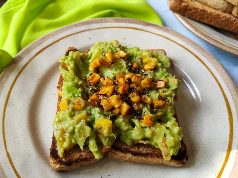 vegan avocado toast with pineapple and sweetcorn served on a plate kept on a bright green table napkin