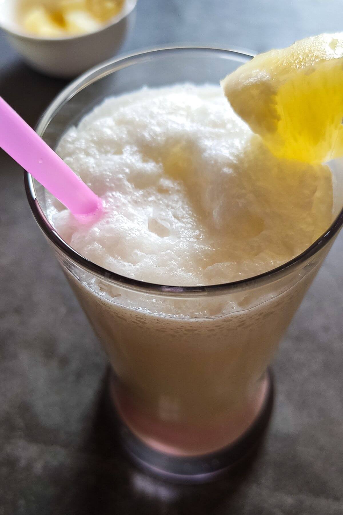 virgin pina colada garnished with a pineapple chunk and a pink straw.