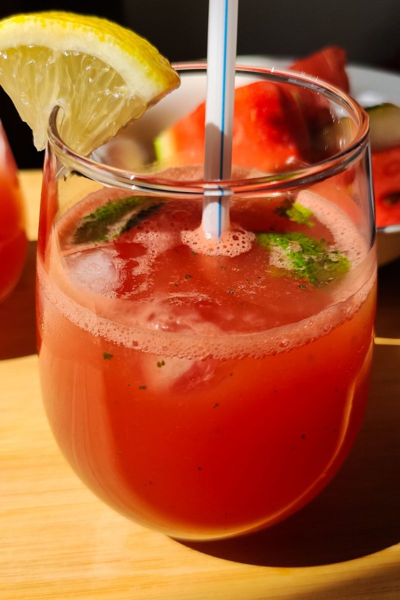 watermelon lemonade served in glass with a white straw and garnished with mint leaves and a lemon wedge.