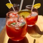 Three glasses of watermelon lemonade with white straws, garnished with mint leaves and lemon wedges