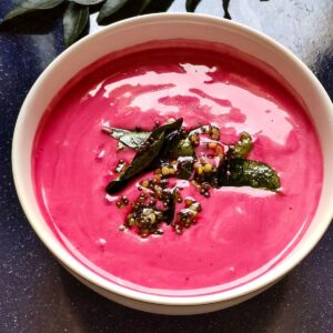 Raita made with beetroot, tempered with curry leaves and mustard seeds served in a white bowl