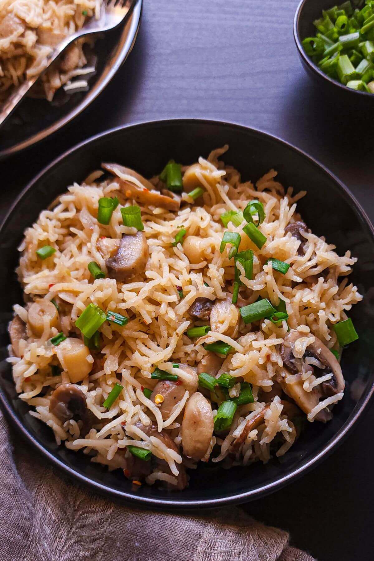 Mushroom rice garnished with chopped spring onion served on a black wok