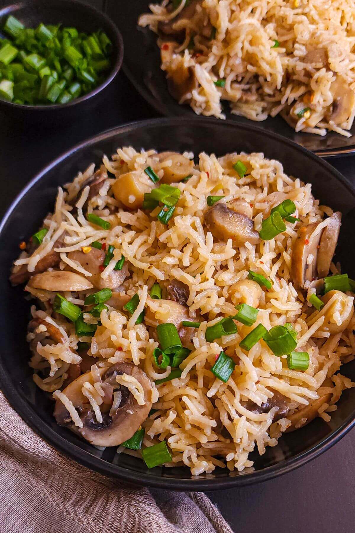 Mushroom rice garnished with chopped spring onion served on a black bowl