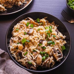 A bowl of mushroom rice garnished with chopped spring onion greens.