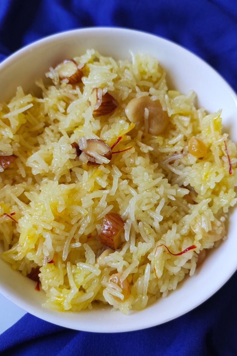 Indian style sweet rice garnished with dry fruits served in a white bowl kept on a blue table napkin