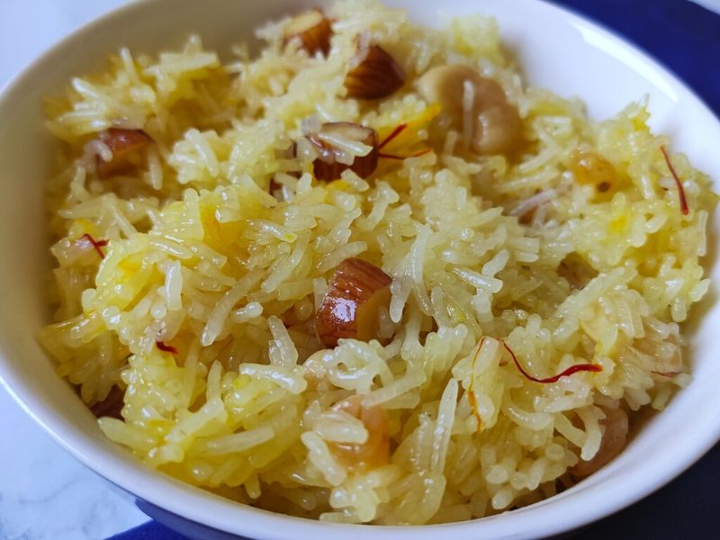 Indian style sweet rice garnished with dry fruits served in a white bowl kept on a blue table napkin