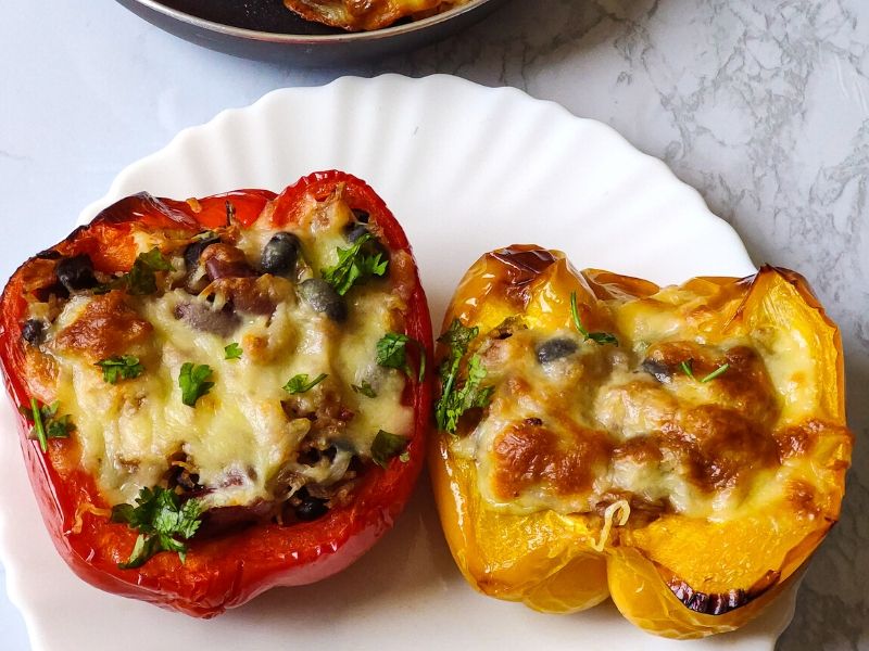 One red and one yellow stuffed bell pepper kept on a white plate