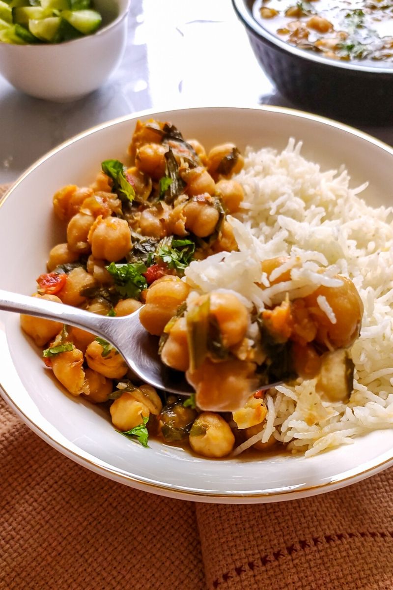 Chickpea spinach curry served with rice in a shallow white bowl and a spoon full of curry and rice lifted above the bowl