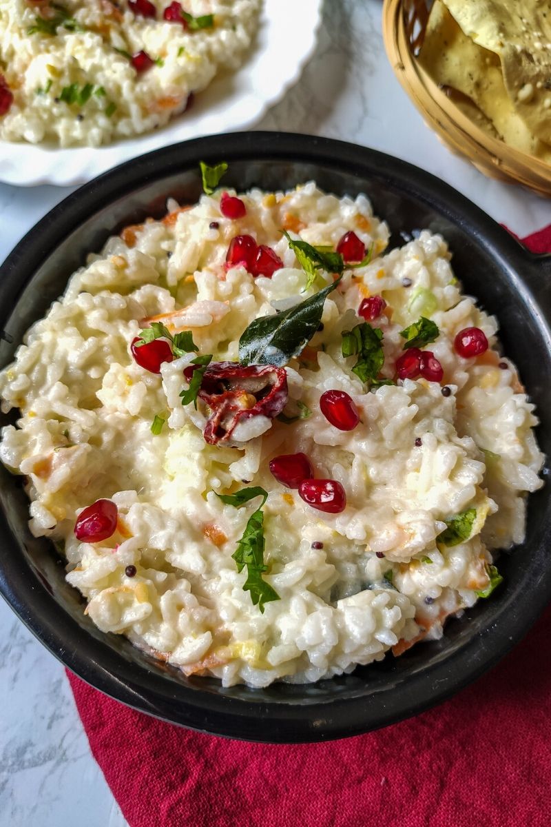 curd rice garnished with pomegranate seeds served in a black bowl kept on a red table napkin