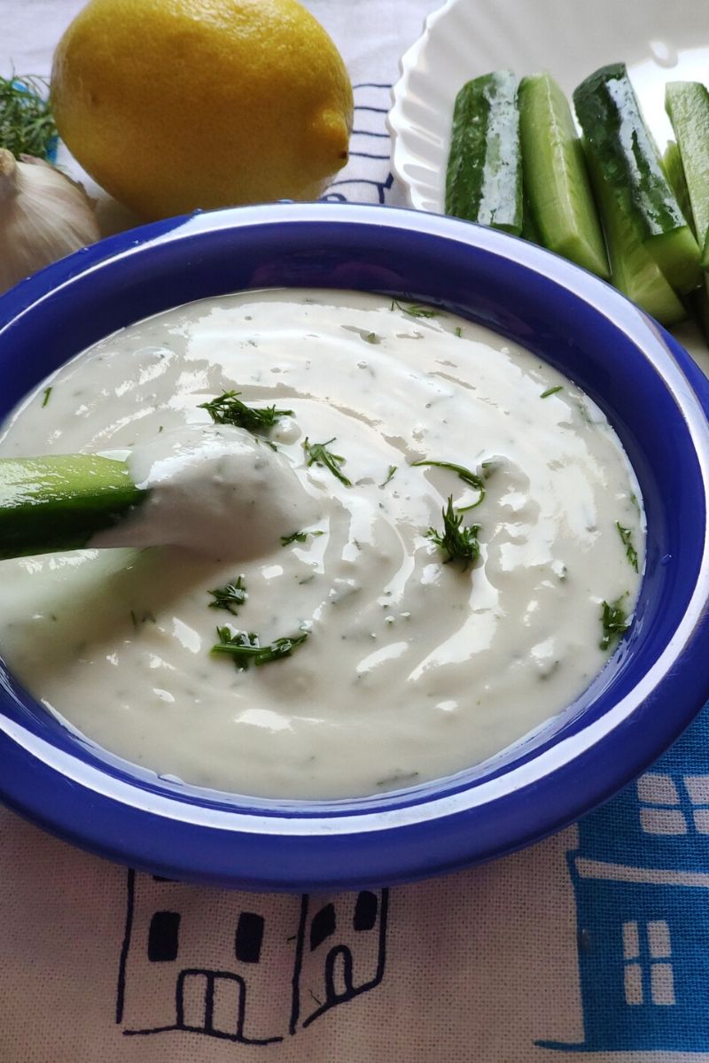 Greek yogurt dip served in a blue bowl with a lemon and cucumber sticks in the background