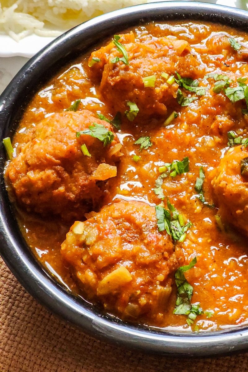 lauki ke kofte garnished with coriander leaves served in a black bowl with some rice in the background