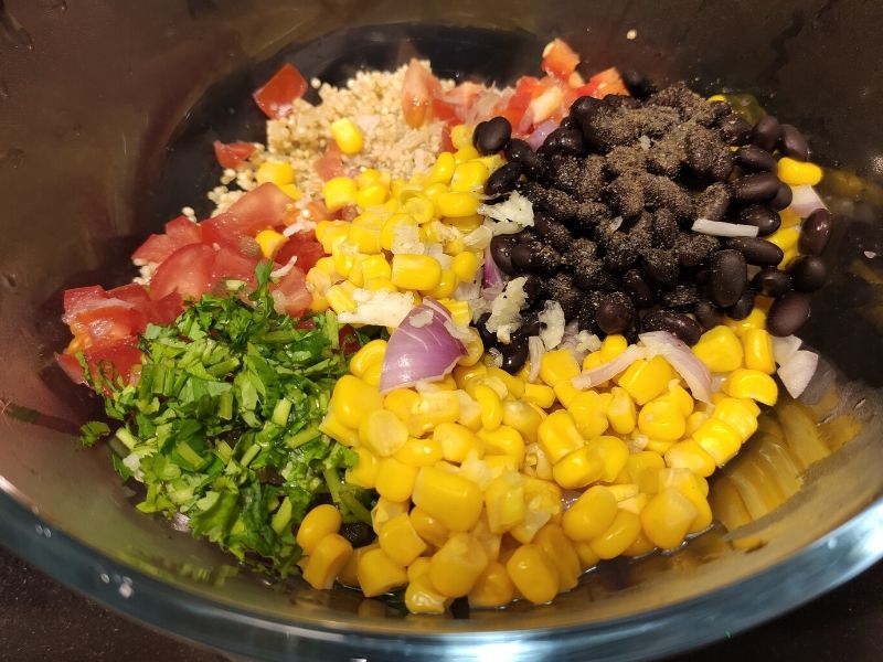Black beans, corn, herbs, chopped bell peppers, quinoa, and other ingredients of corn salad kept in a glass bowl