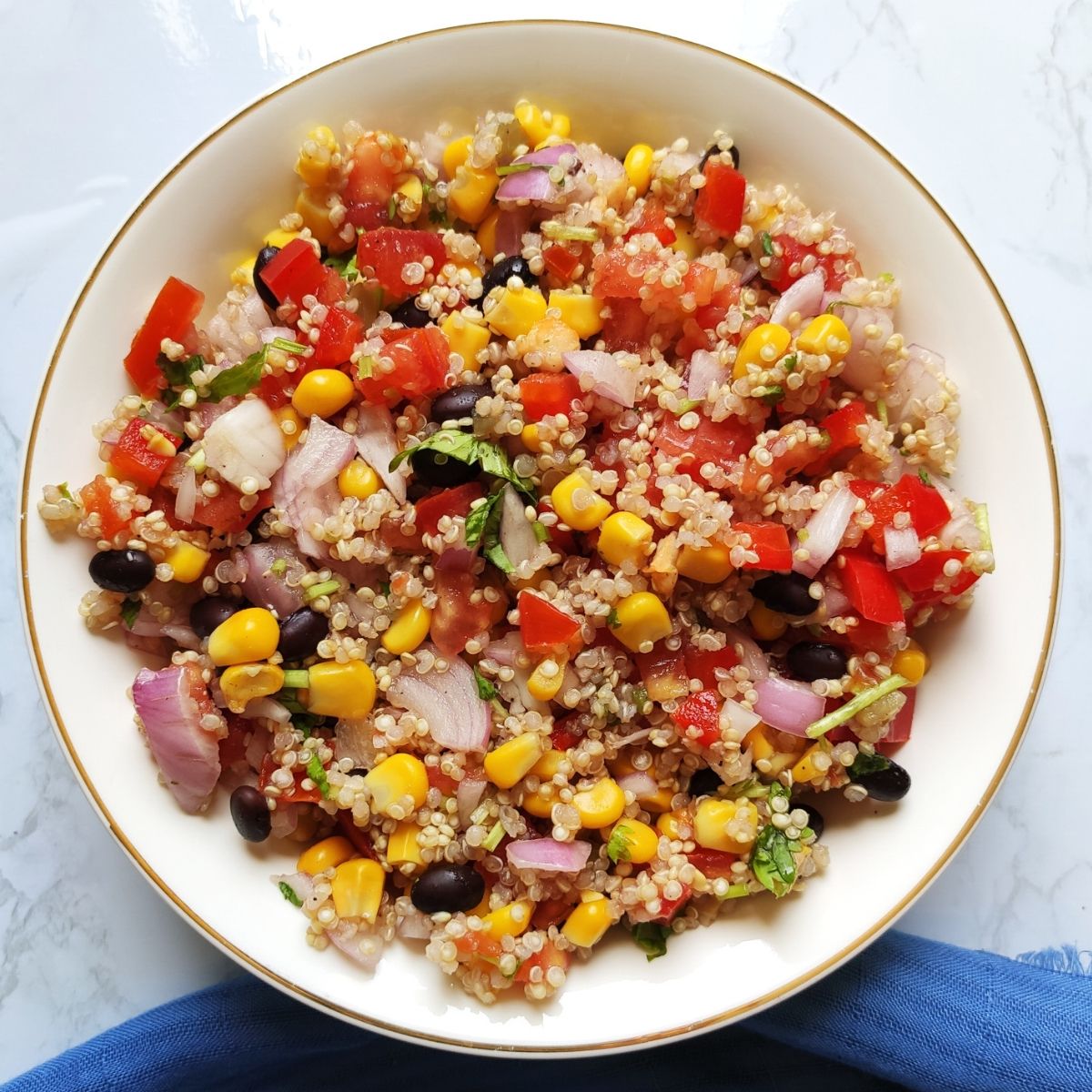 Mexican corn quinoa salad served in a white bowl kept on a blue table napkin