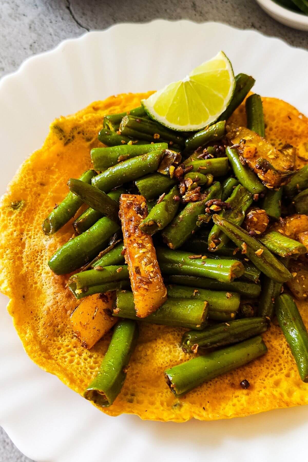 Indian style green beans and potato served on top of Indian pancakes with a lime wedge.