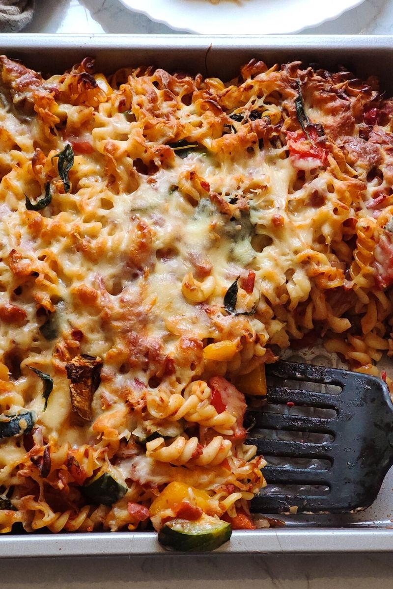 Baked vegetarian pasta getting scooped out with a black spatula