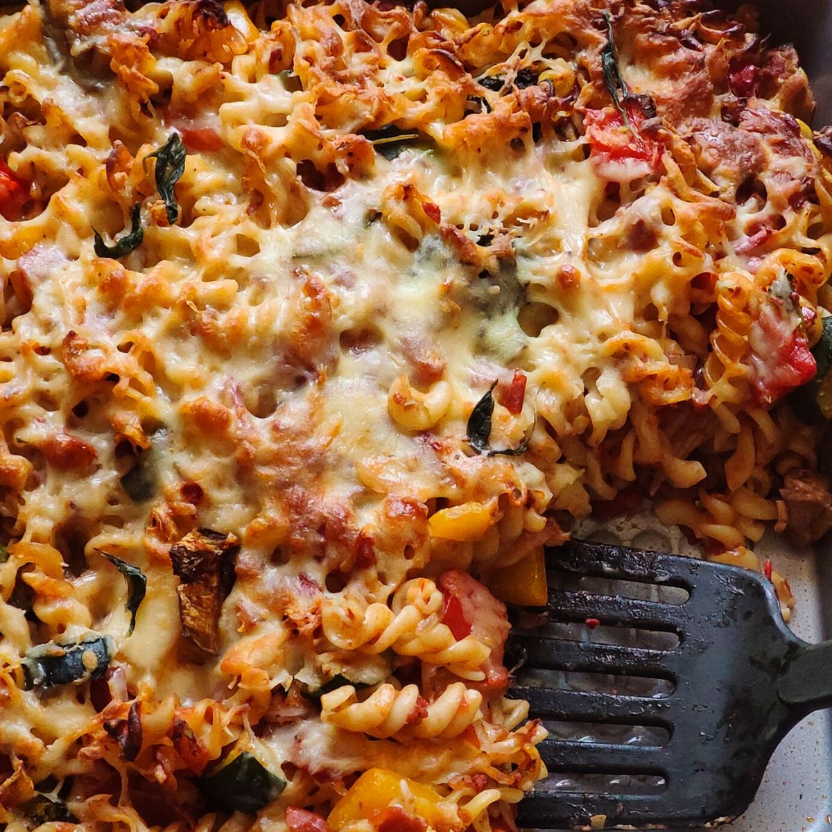 Vegetable baked pasta getting scooped out with a black spatula
