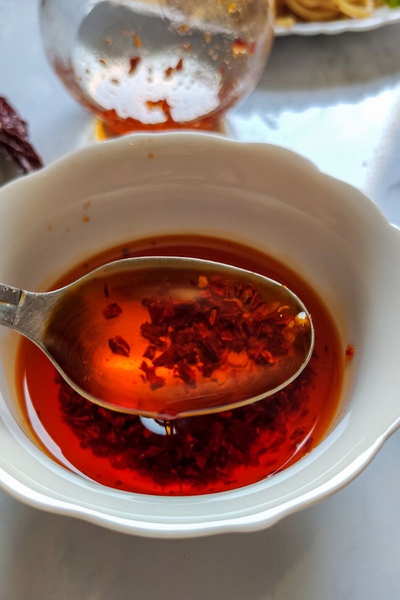 A spoon full of chili oil lifted above a white bowl of chili oil