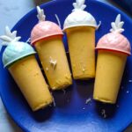 Four vegan popsicles with pineapple shaped mold sticks served on a blue plate