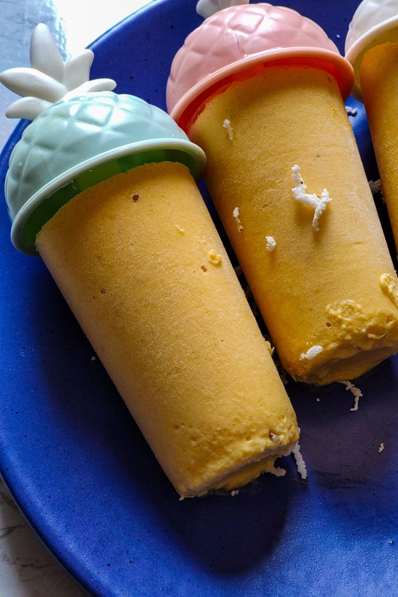 two tropical popsicle garnished with grated coconut served on a blue plate