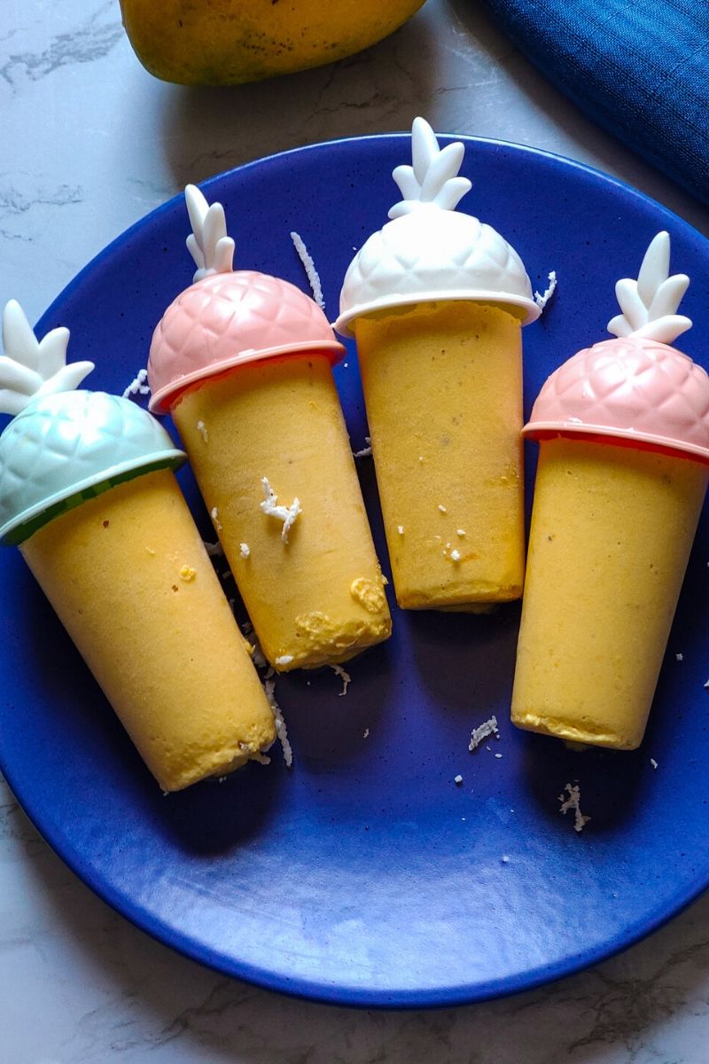 Four Tropical popsicles served on a blue plate with a part of mango and blue table napkin visible in the background