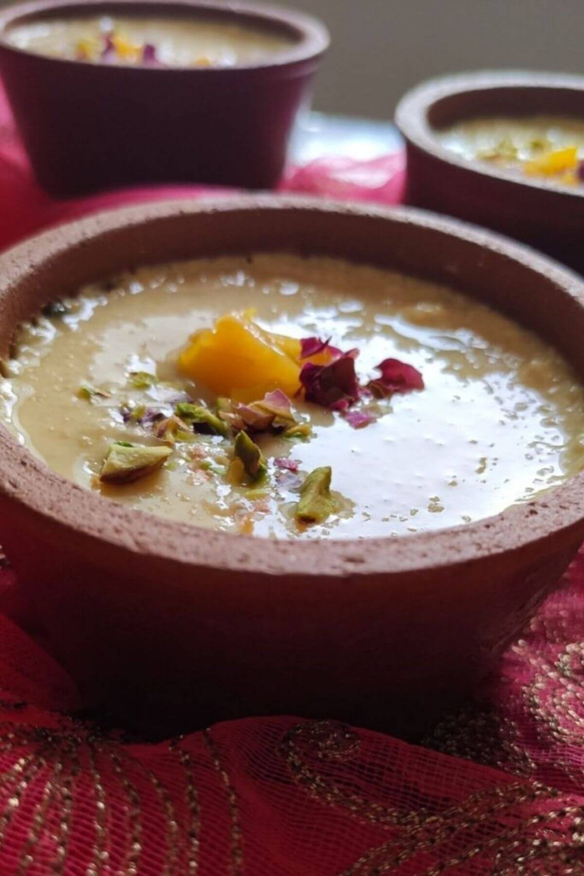 Mango phirni garnished with chopped mango, rose petals, and nuts served in an earthen pot