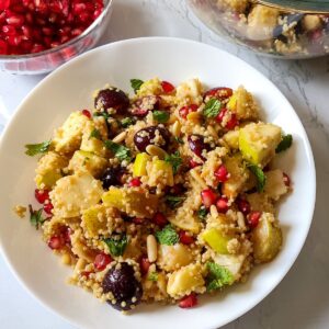 Quinoa fruit salad served on a white plate with pomegranate seeds in the background
