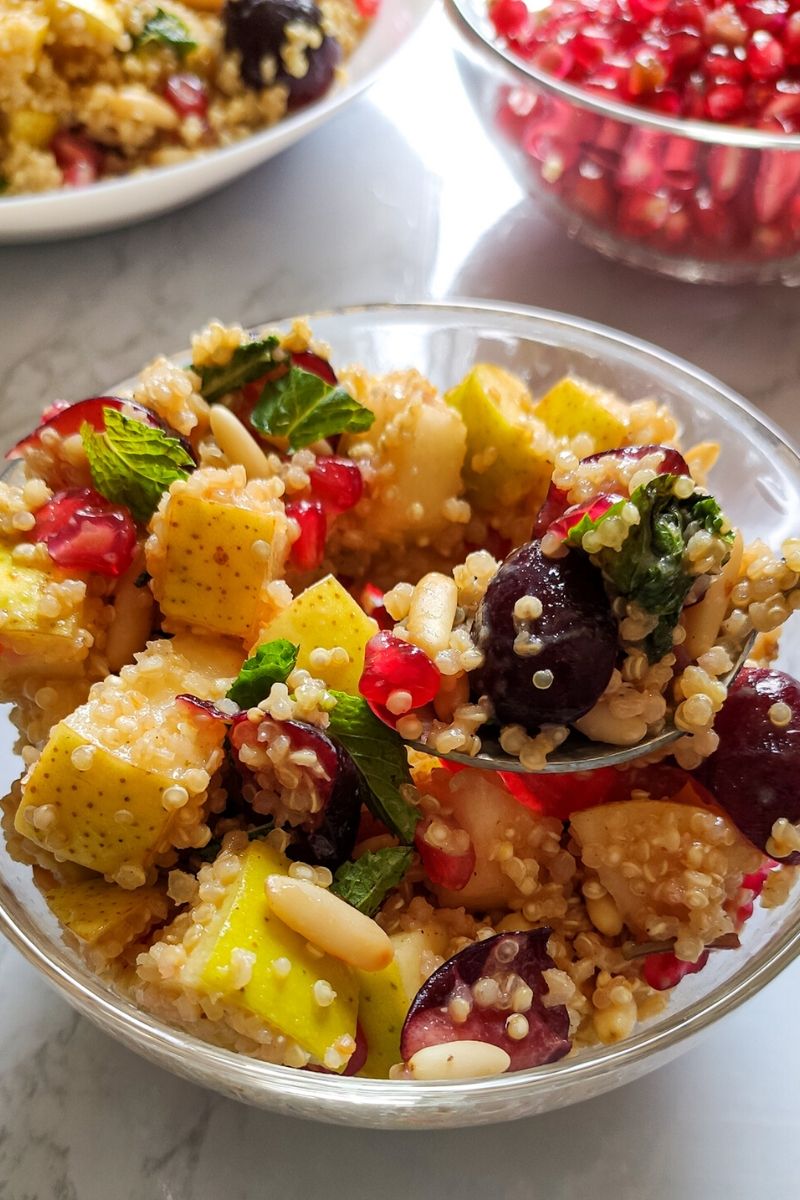 Quinoa fruit salad served on a white plate with pomegranate seeds in the background