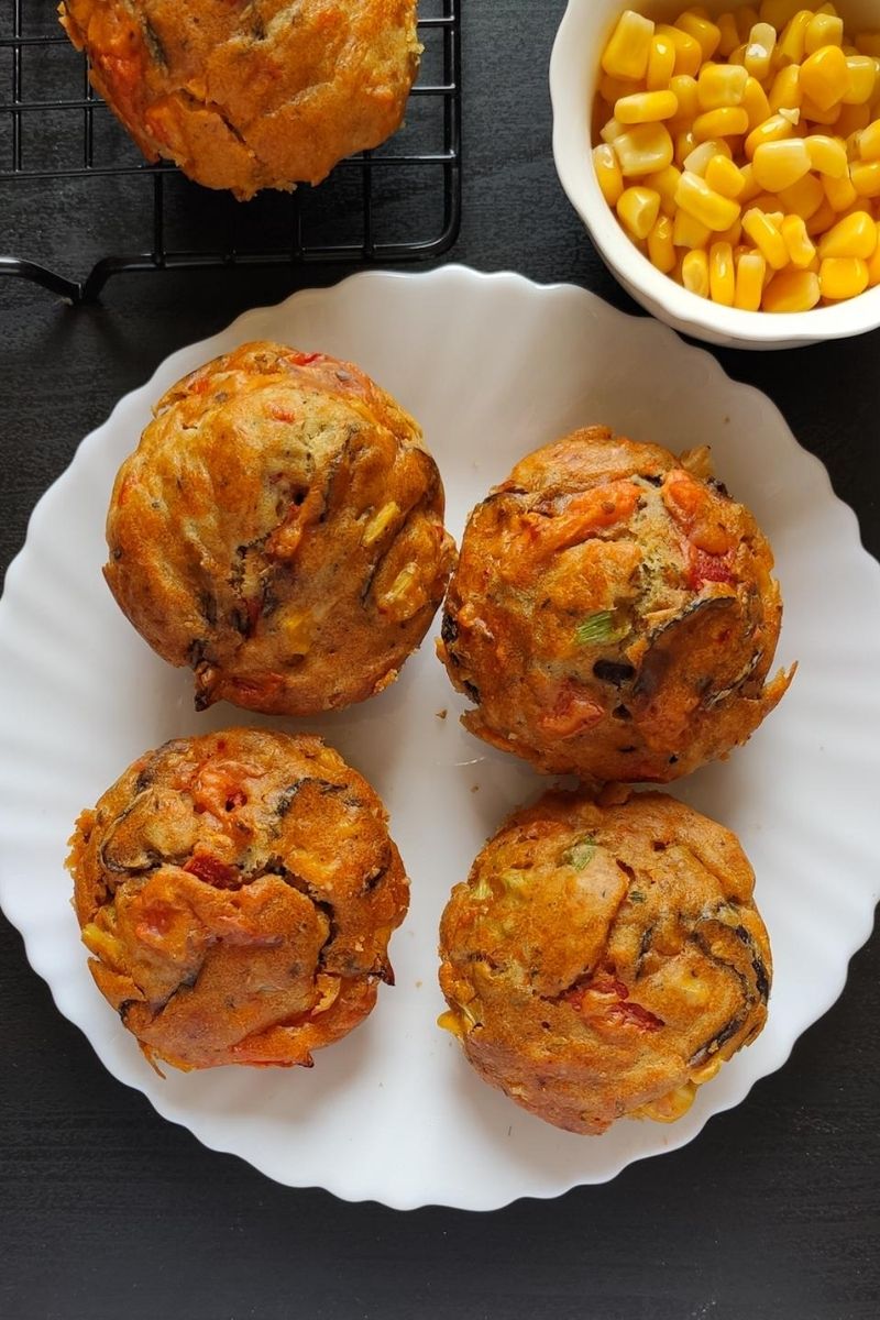 four savoury muffins kept on a whote plate with some corn kernels in the background