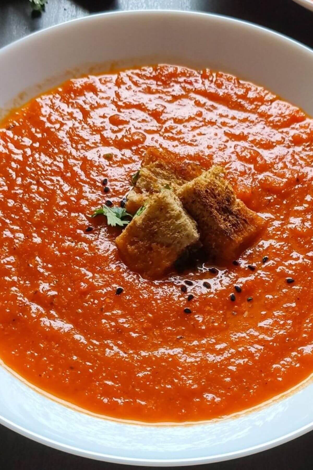 Close up shot of tomato bell pepper soup garnished with croutons and black seeds