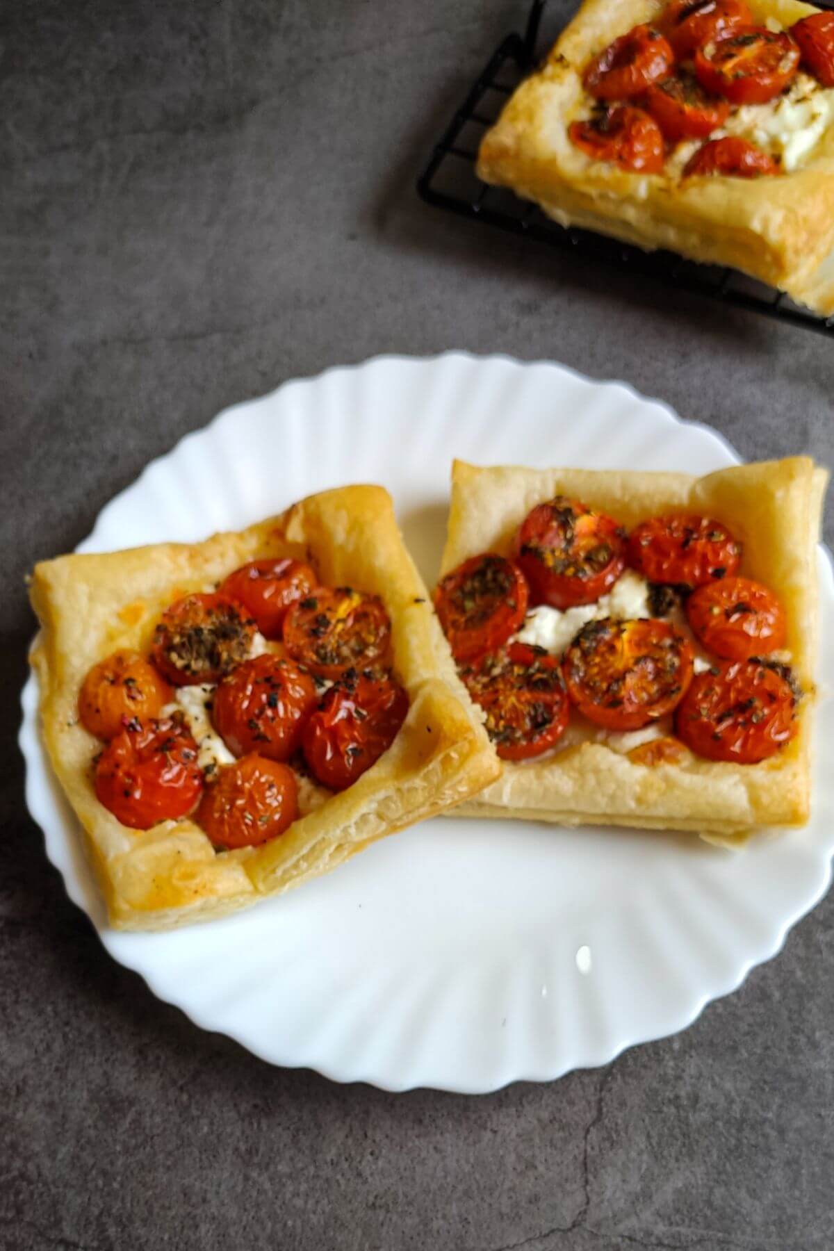 Two tomato puff pastries on a white plate and another pastry in the background.