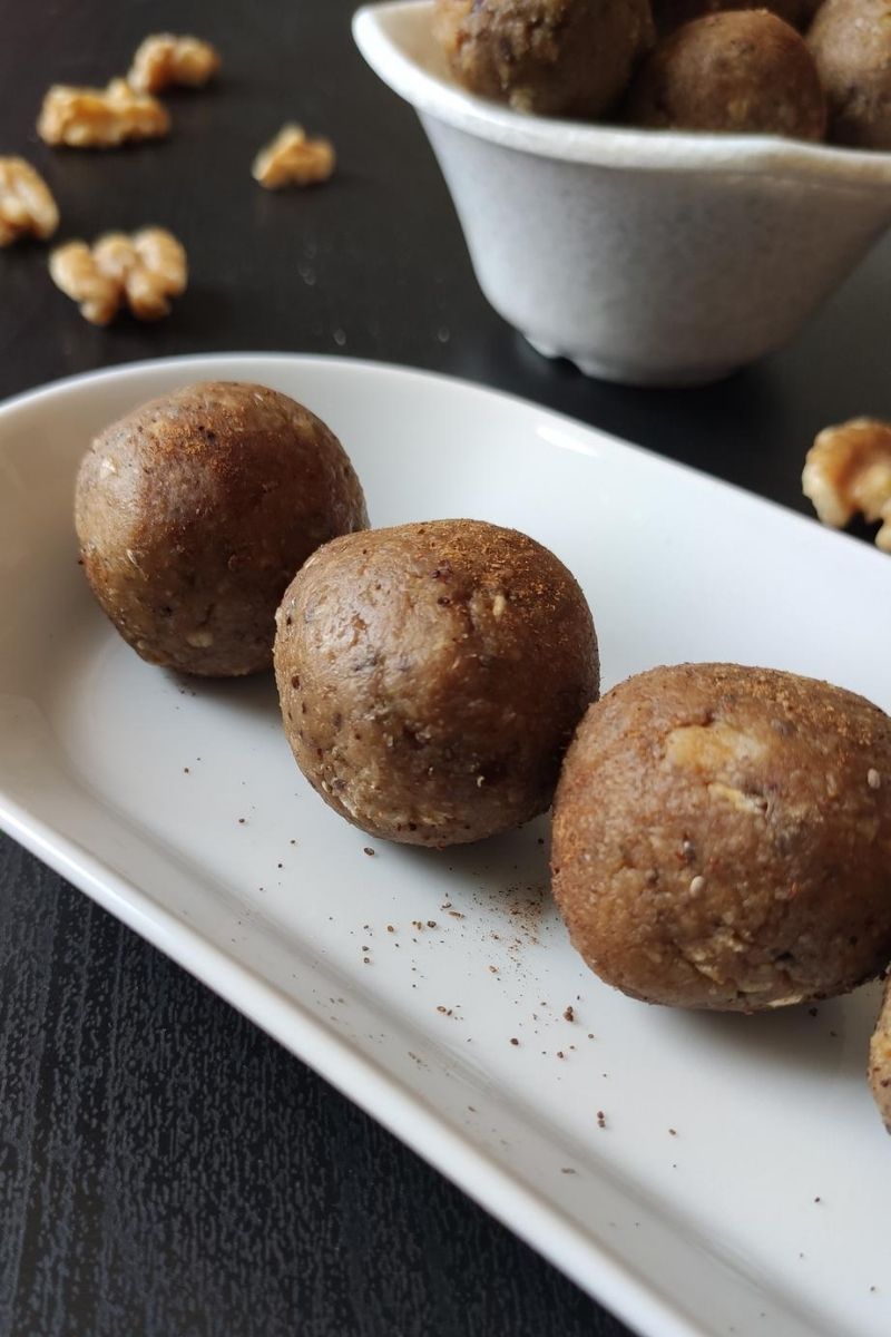 vegan energy balls served on a white snack plate and more kept in a bowl in the background