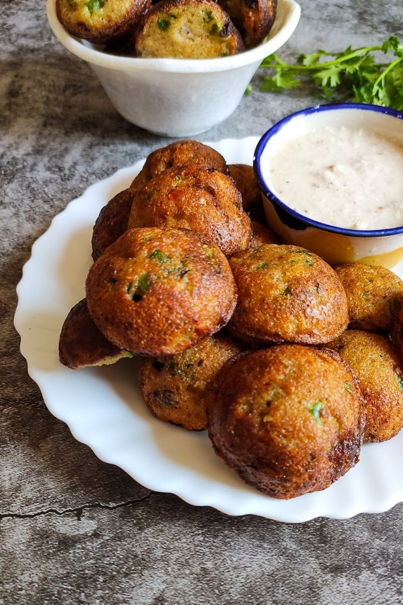 Vegetable paniyaram serve on a white plate with coconut chutney more paniyram in the background