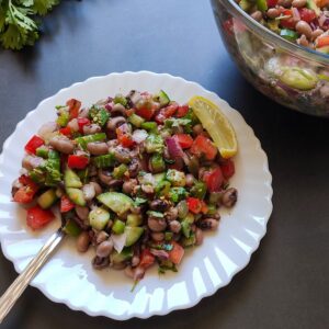 black eyed pea salad on a white plate with a bowl of salad and herbs in the background