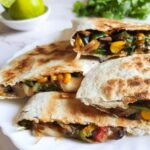 Veggie quesadillas on a white plate with herbs and limes in the background.
