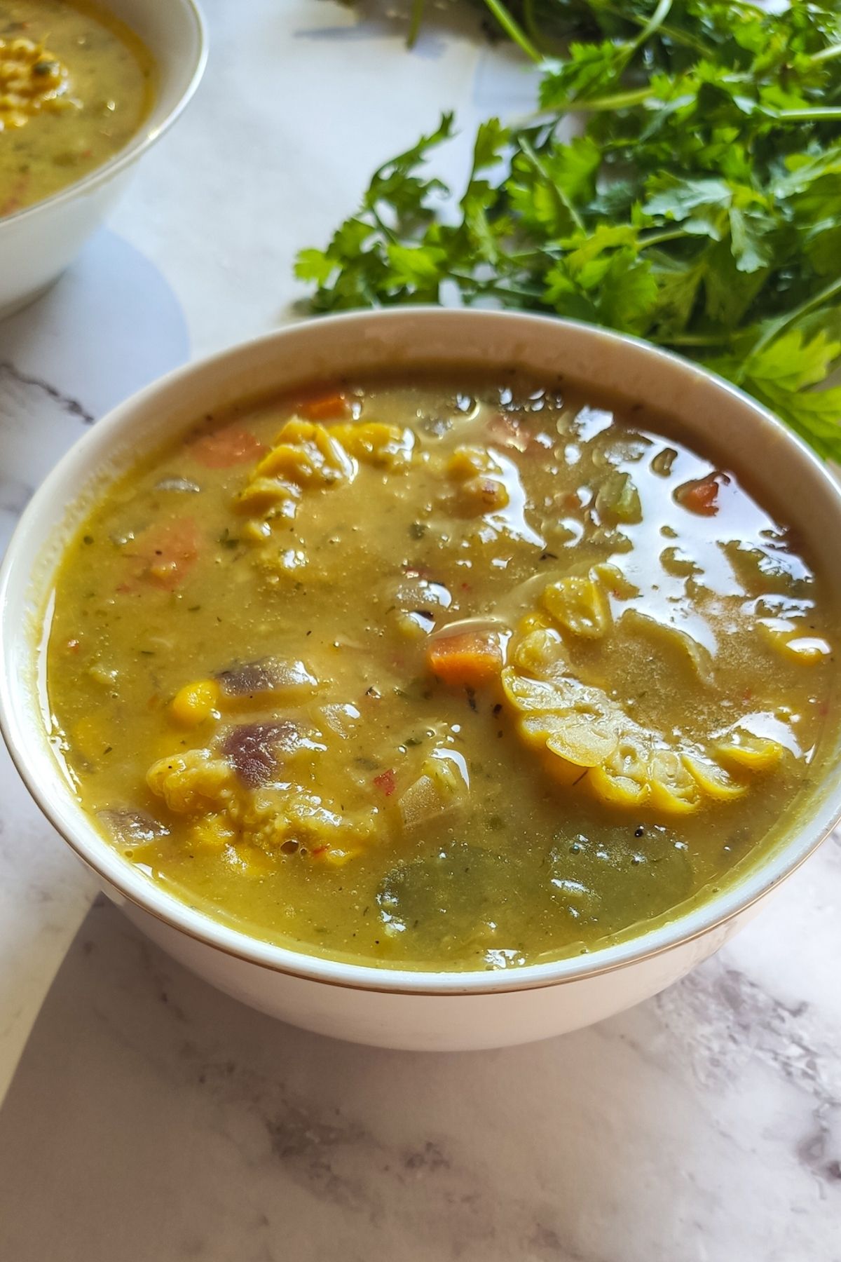 Trinidad corn soup in a white bowl with cilantro in the background