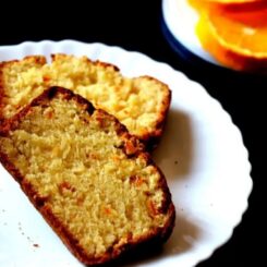 Two slices of vegan orange cake on a white plate with slices of orange in the background