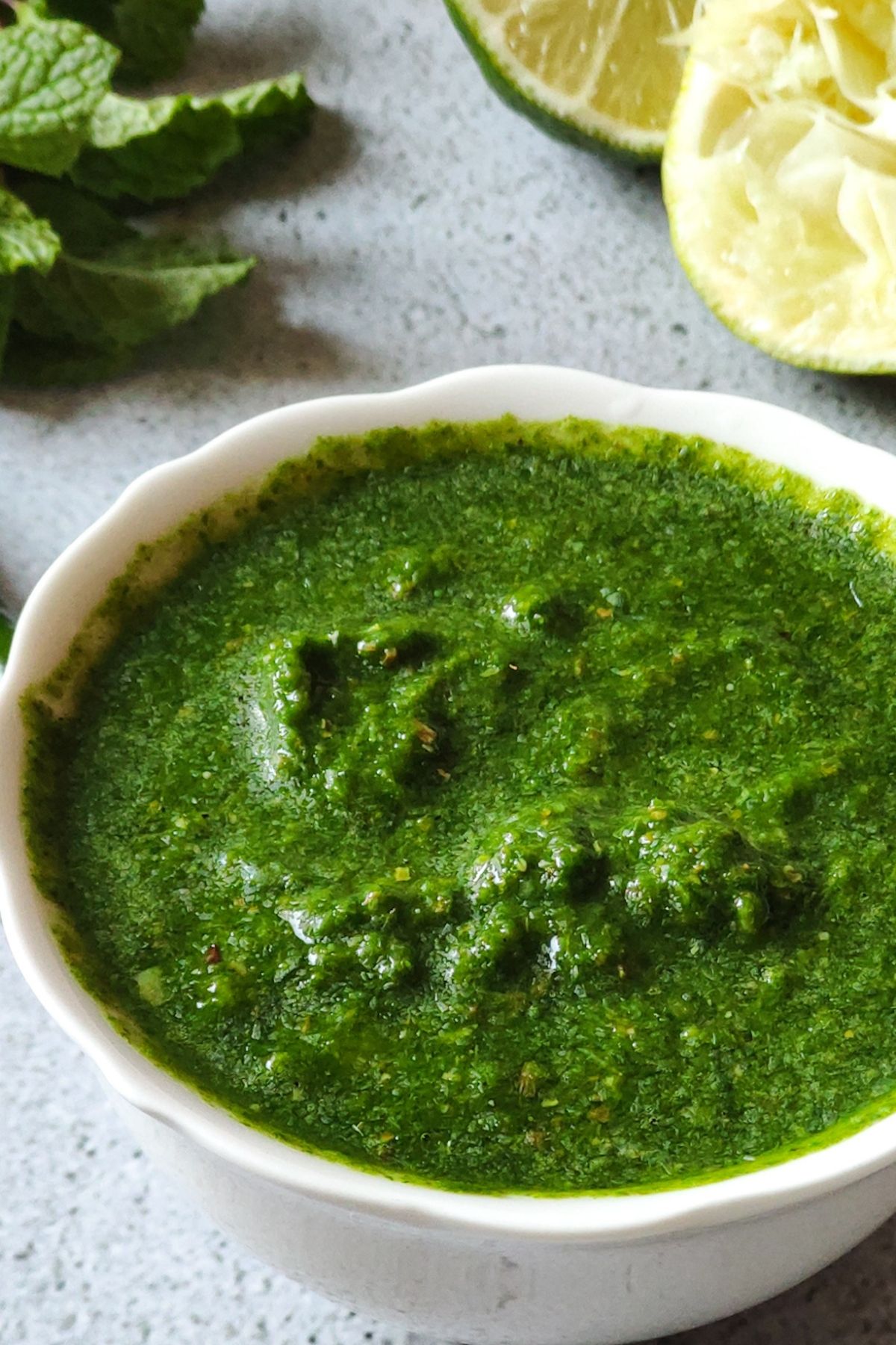 green mint chutney in a white bowl with lime and mint leaves in the background