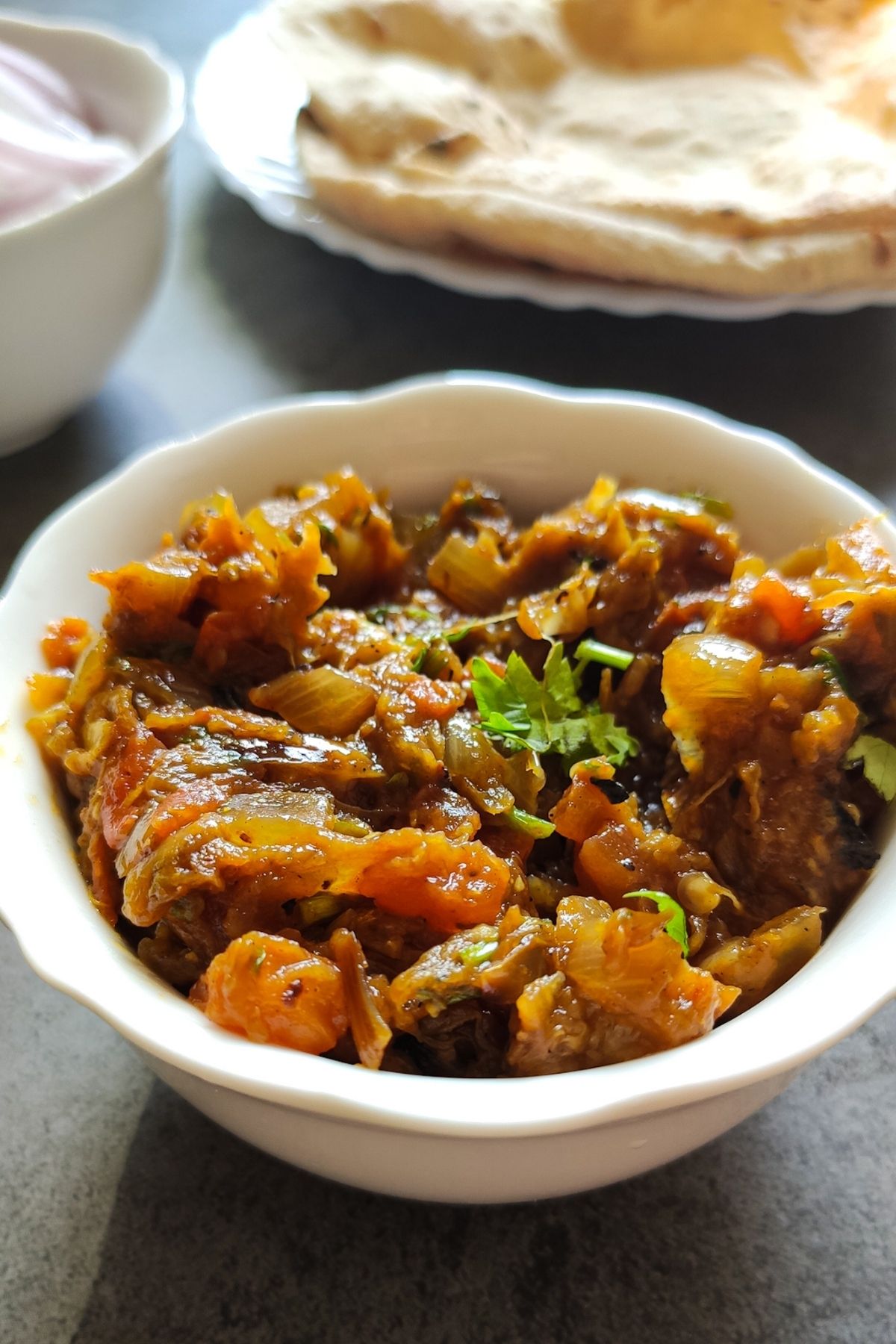 Baingan bharta in a bowl with chapati and salad in the background