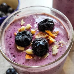 A glass of blueberry banana smoothie garnished with blueberries and nuts