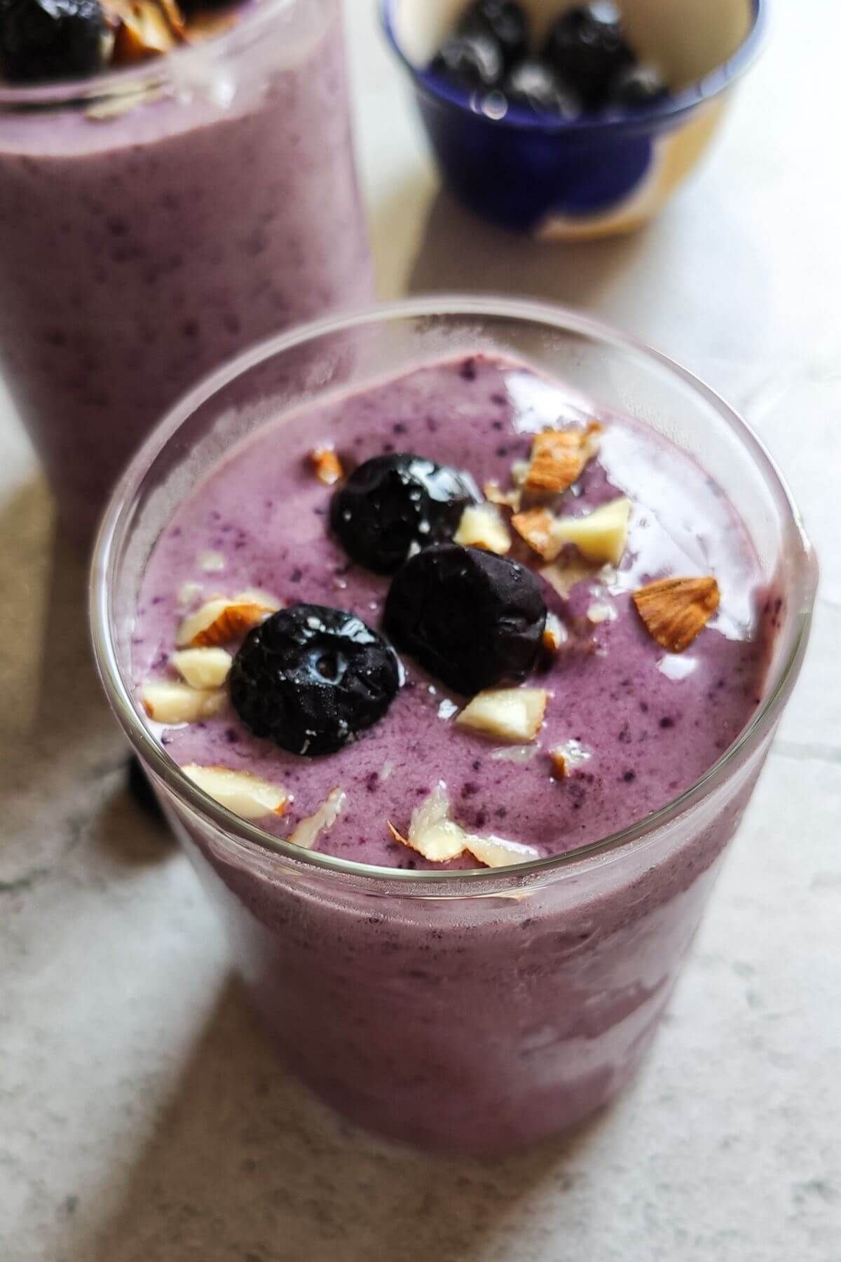 A glass of blueberry banana smoothie another glass in the background