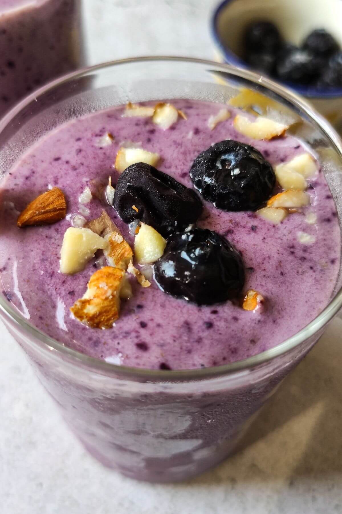 A glass of blueberry smoothie garnished with blueberries and nuts