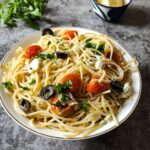Vegetarian Greek spaghetti in a white bowl with herbs and lemon in the background