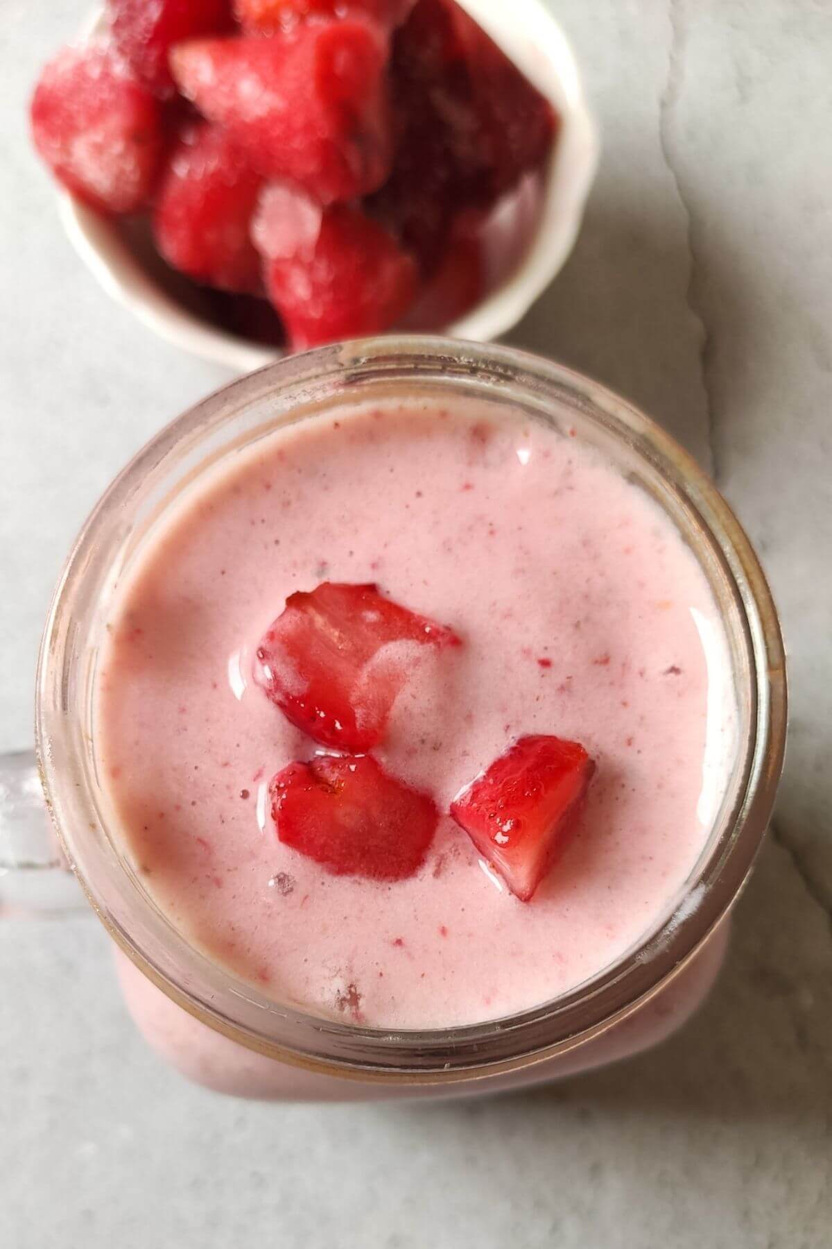 Healthy strawberry banana smoothie in a jar with a bowl of strawberries in the background