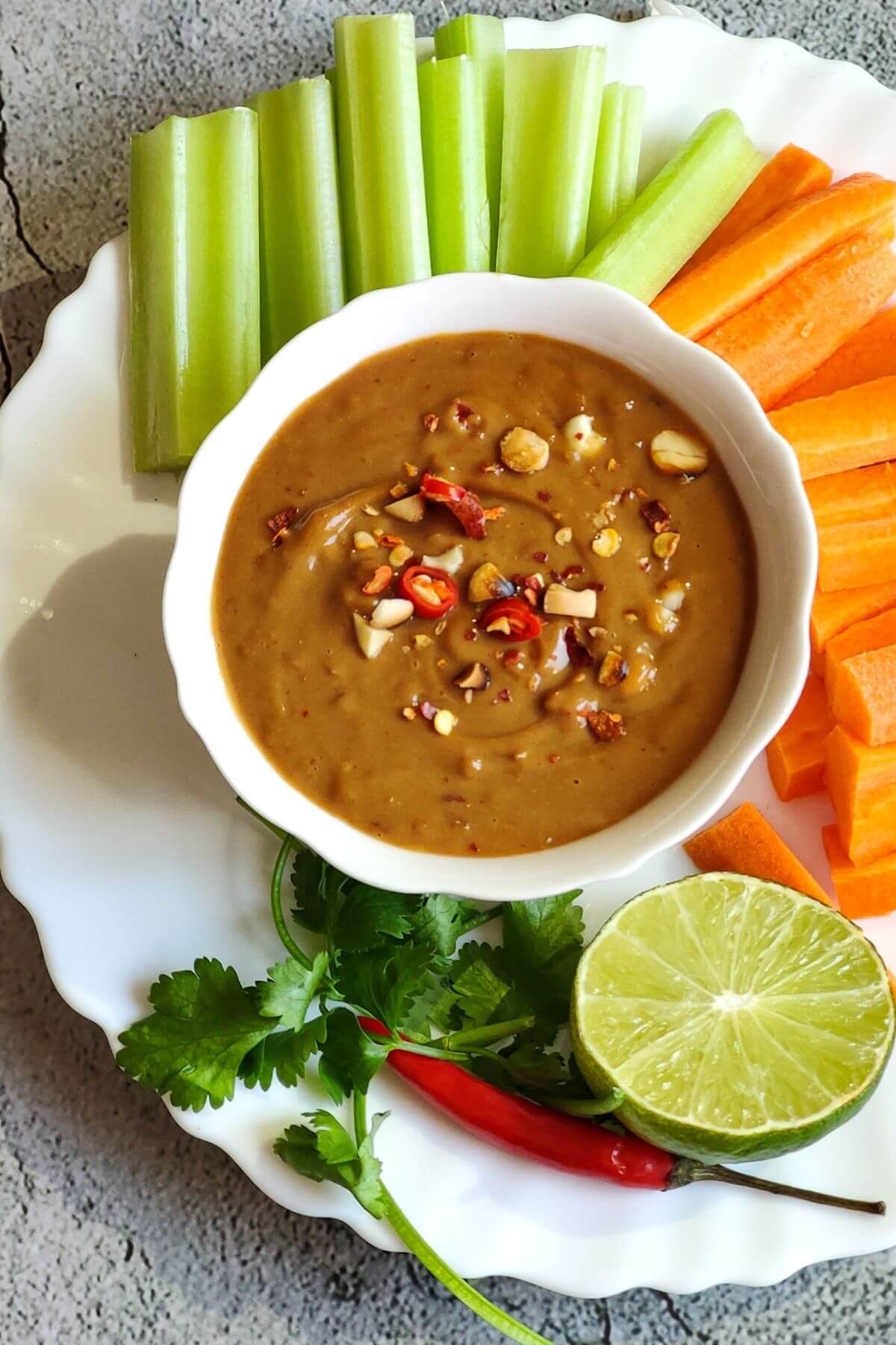 Thai peanut sauce served with vegetable sticks, lime slice, chili pepper, and cilantro